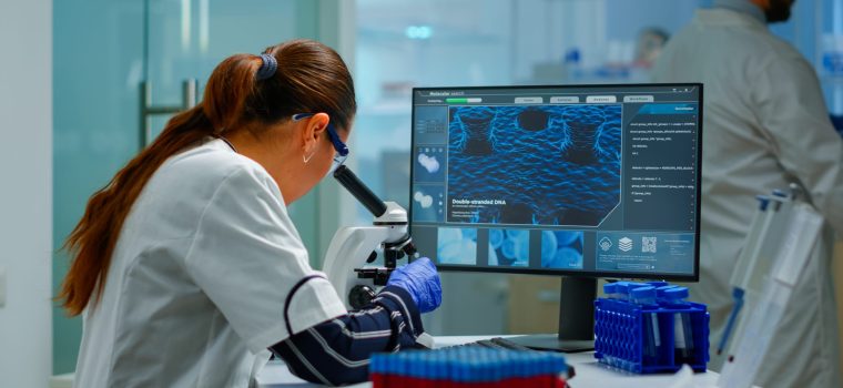Biotechnology scientist researching in laboratory using microscope and typing on pc. Chemist examining virus evolution using high tech for scientific research of vaccine development against covid19